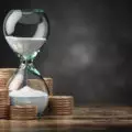 Gold coins stacked in ascending order next to an hour glass