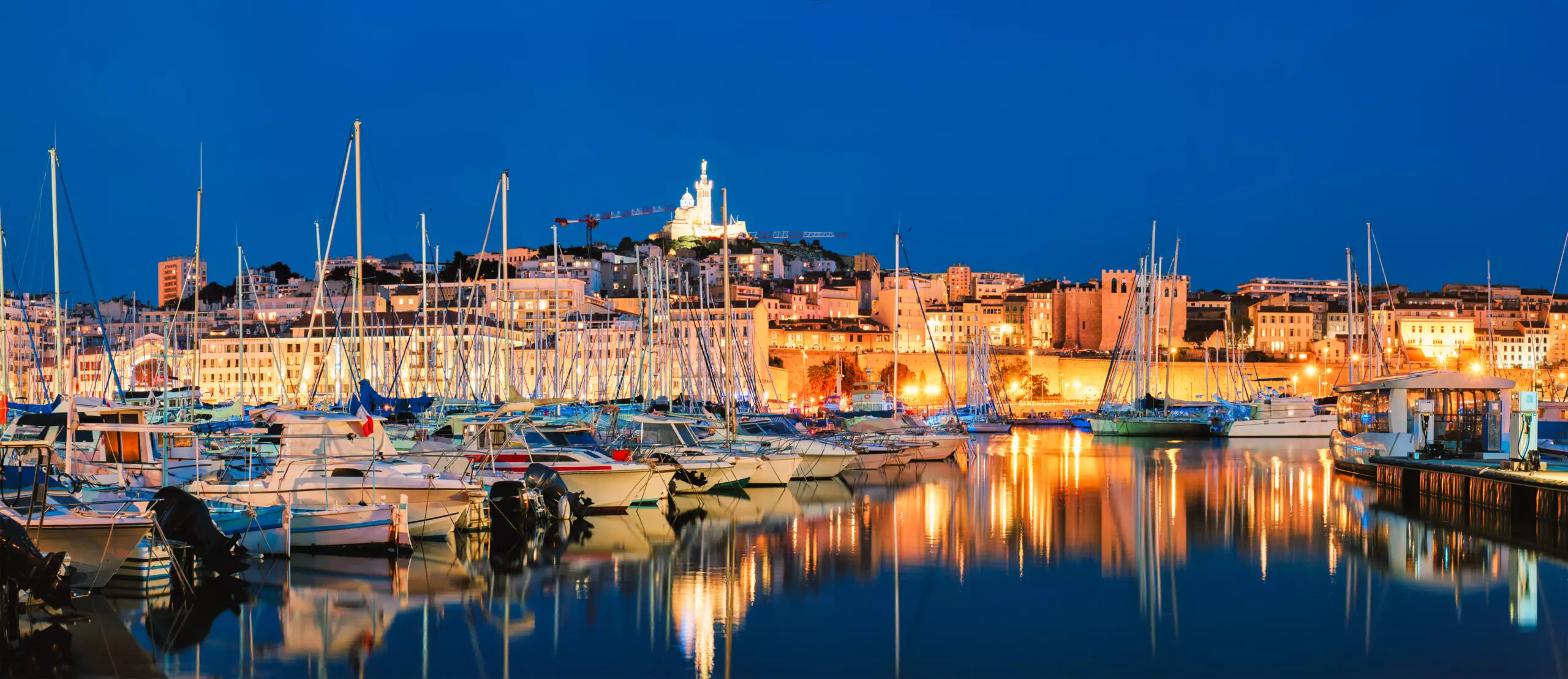 Panorama of Marseille Old Port (Vieux-Port de Marseille) with yachts and Basilica of Notre-Dame de la Garde in the night. Marseille, France